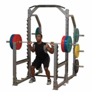 Rack à Squat Multifonctions BODYSOLID Pro Club Line. On voit un homme en train de squatter une barre avec plusieurs disques de poids dessus.